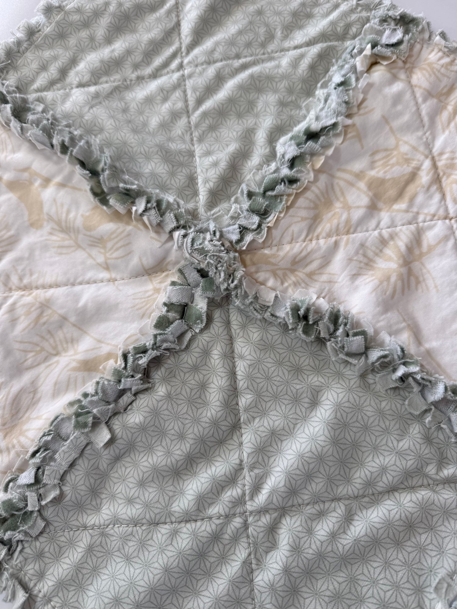 Close-up of a quilt with ruffled edges in teal and cream bird pattern. 