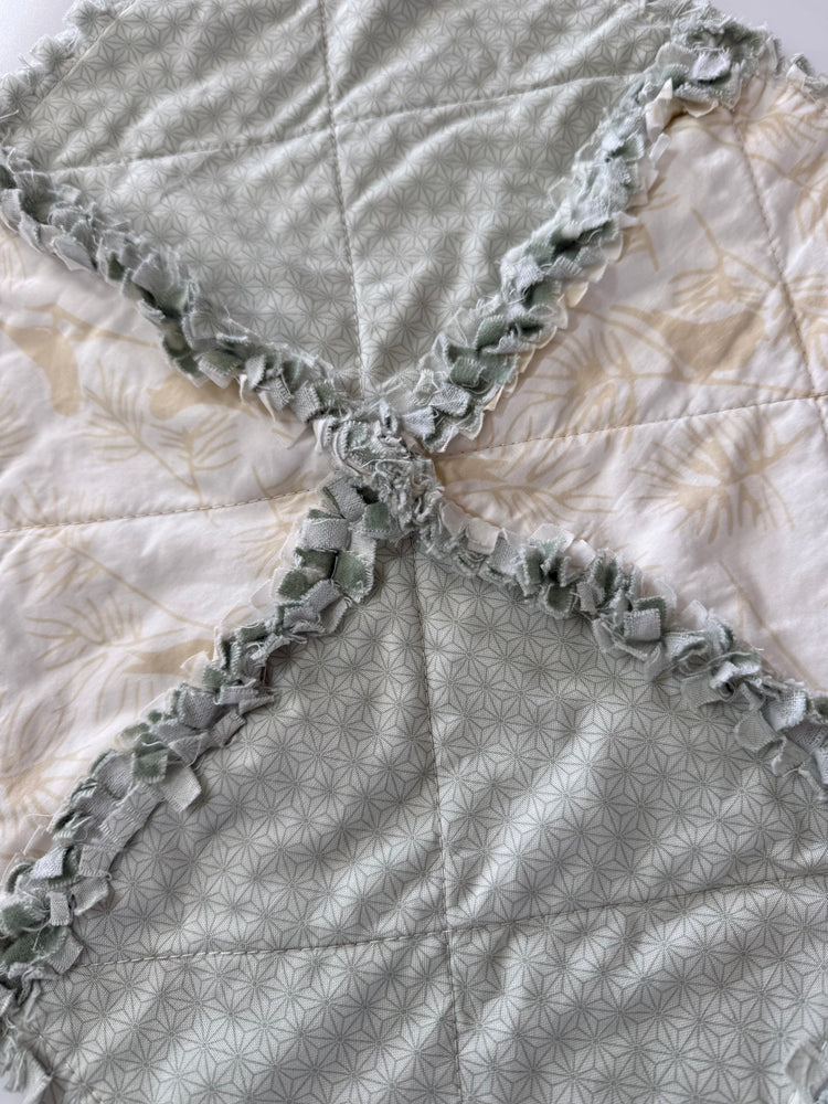 Close-up of a quilt with ruffled edges in teal and cream bird pattern. 