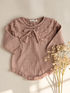 A dusty rose pink knit long-sleeve top for toddlers, featuring a ruffled collar with a bow, textured knit pattern, and decorative buttons along the hem. The top is displayed flat on a light beige background next to dried baby&