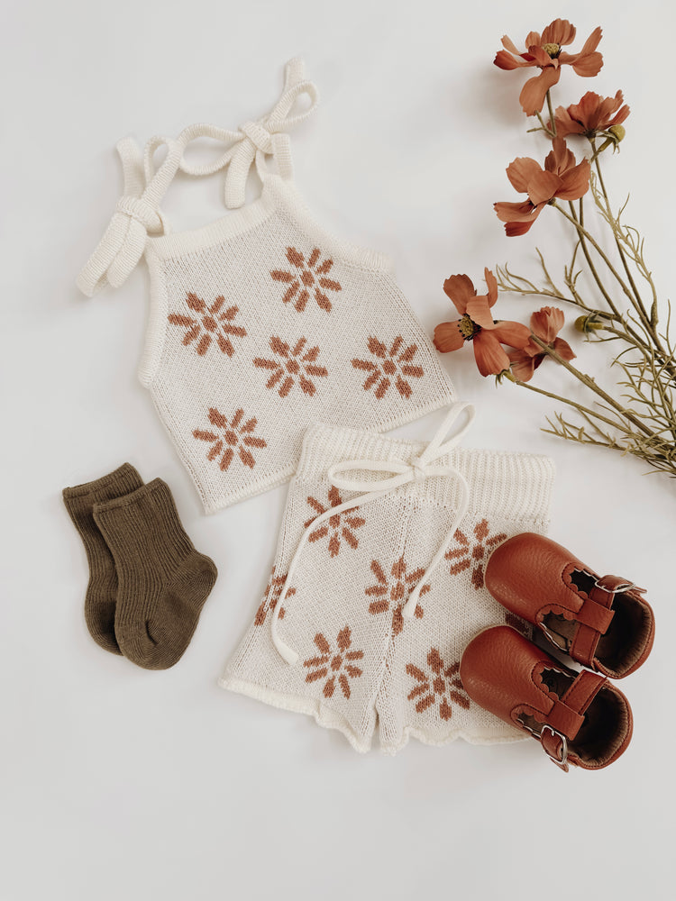 Baby knitted romper with terracotta colored floral designs, socks, and shoes on a light background