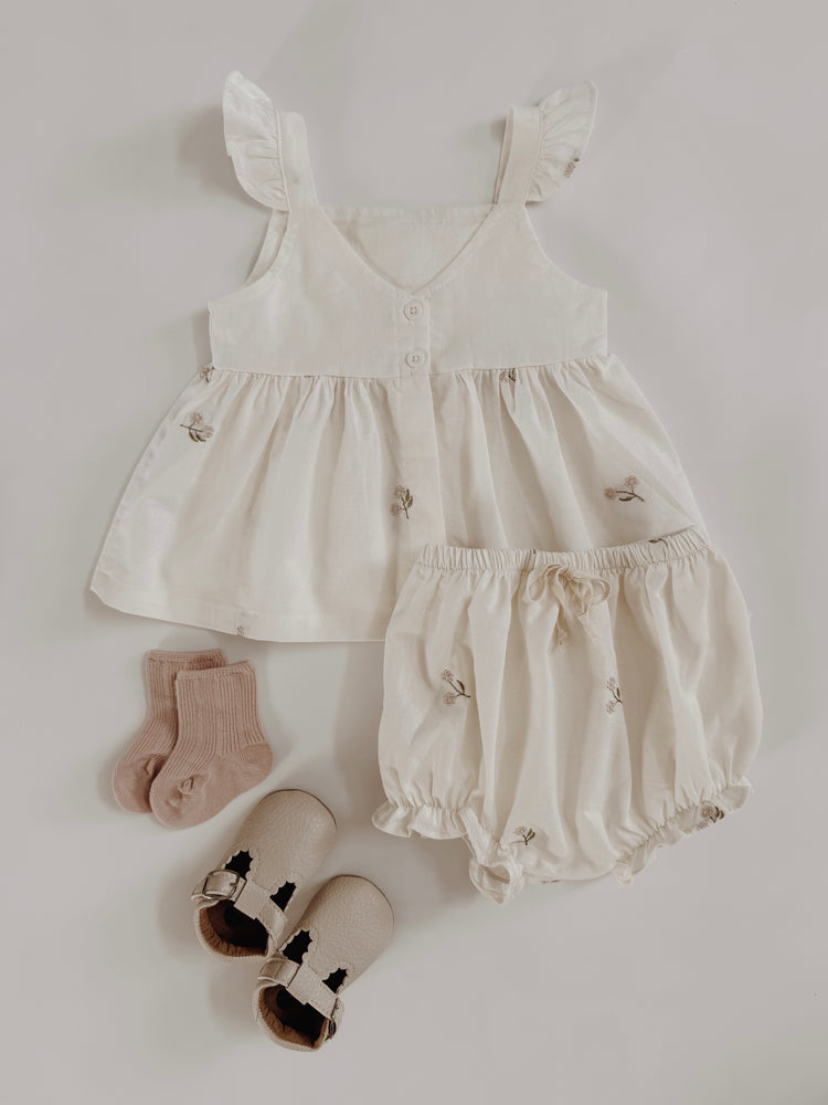 Baby outfit set with dress, bloomers, and socks on a light gray background