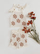 Knitted top and shorts set with terracotta floral patterns on a white background with flowers.