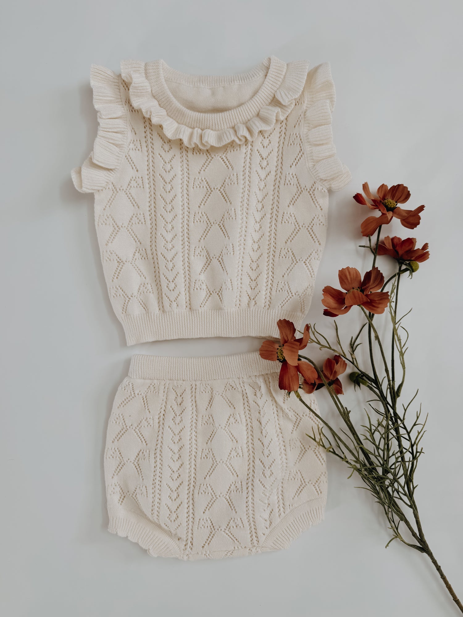 Knitted outfit with ruffled top and cable knit skirt on a white background with flowers.
