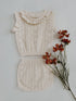 Knitted outfit with ruffled top and cable knit skirt on a white background with flowers.